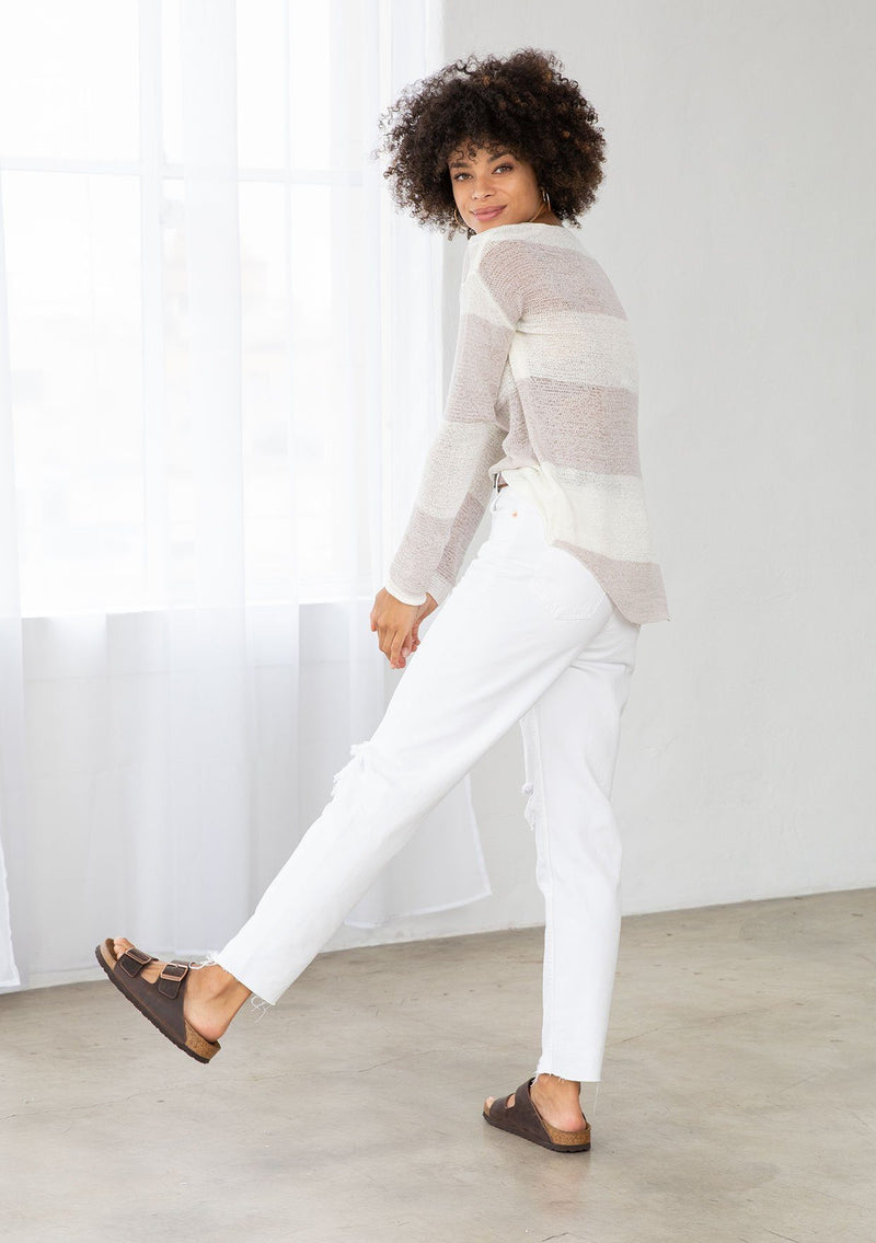 [Color: Silver/Ivory] A model wearing a silver and ivory color block stripe sweater. With a wide v neckline, long sleeves, a dropped shoulder, and a high low hemline. 