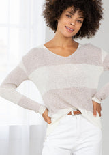 [Color: Silver/Ivory] A model wearing a silver and ivory color block stripe sweater. With a wide v neckline, long sleeves, a dropped shoulder, and a high low hemline. 