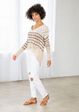 [Color: Ivory/Cement] A model wearing an ivory and sand striped color block lightweight bohemian beach sweater. With an open tie back detail, long sleeves, a dropped shoulder, and a high low hemline.