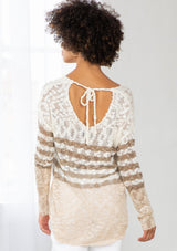 [Color: Ivory/Cement] A model wearing an ivory and sand striped color block lightweight bohemian beach sweater. With an open tie back detail, long sleeves, a dropped shoulder, and a high low hemline.