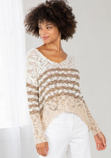 [Color: Ivory/Cement] A model wearing an ivory and sand striped color block lightweight bohemian beach sweater. With an open tie back detail, long sleeves, a dropped shoulder, and a high low hemline.