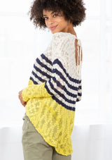 [Color: Ivory/Navy] A model wearing an ivory and navy striped color block lightweight bohemian beach sweater. With an open tie back detail, long sleeves, a dropped shoulder, and a high low hemline.
