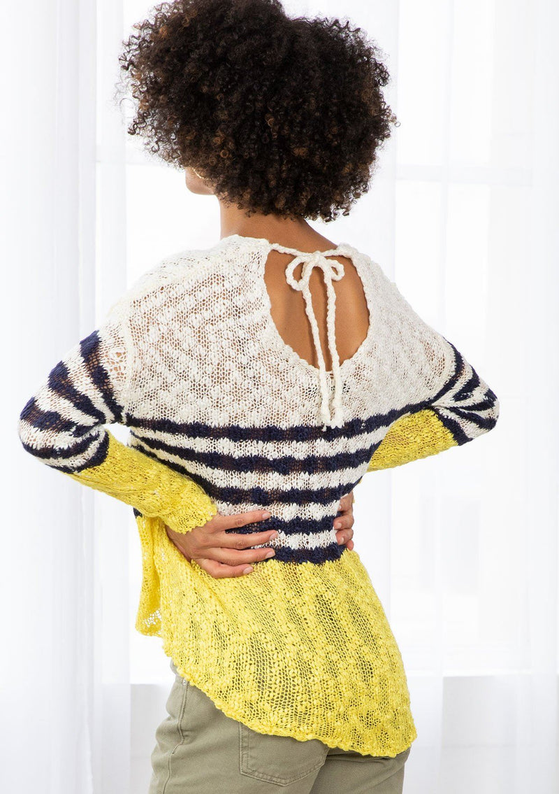 [Color: Ivory/Navy] A model wearing an ivory and navy striped color block lightweight bohemian beach sweater. With an open tie back detail, long sleeves, a dropped shoulder, and a high low hemline.