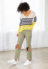 [Color: Ivory/Navy] A model wearing an ivory and navy striped color block lightweight bohemian beach sweater. With an open tie back detail, long sleeves, a dropped shoulder, and a high low hemline.