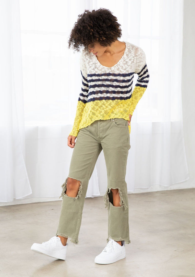 [Color: Ivory/Navy] A model wearing an ivory and navy striped color block lightweight bohemian beach sweater. With an open tie back detail, long sleeves, a dropped shoulder, and a high low hemline.