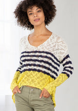 [Color: Ivory/Navy] A model wearing an ivory and navy striped color block lightweight bohemian beach sweater. With an open tie back detail, long sleeves, a dropped shoulder, and a high low hemline.