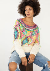 [Color: Ivory/Multi] A model wearing an ivory sweater with bohemian multicolor shaggy yarn yoke detail. With a wide scoop neckline, long sleeves, and a long length. 