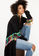[Color: Black/Multi] A model wearing a black chunky knit cardigan with a multicolor shaggy yarn detail. Featuring a fringed waterfall hemline and an open front.