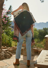 [Color: Floral] A model wearing a red and blue floral sweater poncho with fringed detail and a contrast open knit back. 