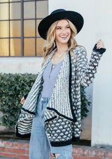 [Color: Black/OffWhite] A blond woman outside wearing an ultra soft chunky marled knit cardigan. Featuring a shawl collar and a contrast trim.