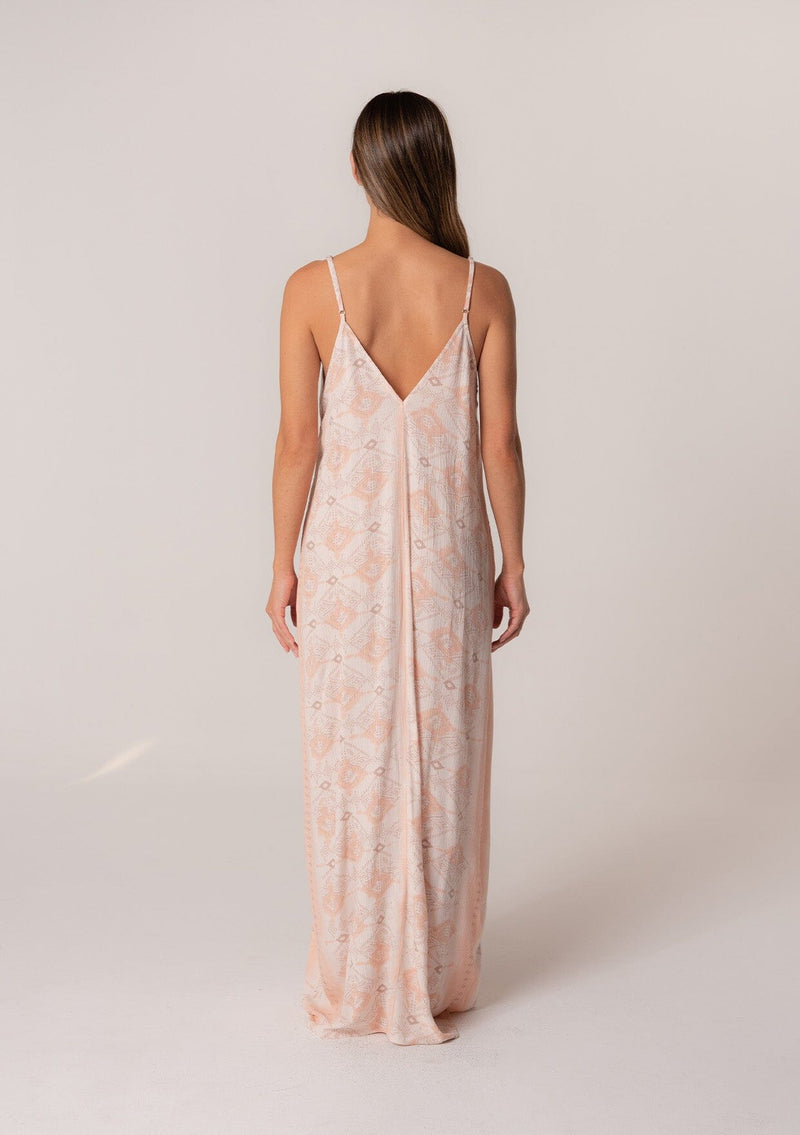 [Color: Natural/Peach] A back facing image of a brunette model wearing a best selling pink bohemian printed maxi dress. With adjustable spaghetti straps, a deep v neckline in the front and back, a flowy, oversize cocoon fit, and side pockets. 