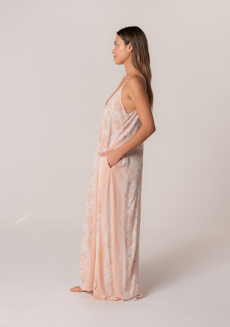 [Color: Natural/Peach] A side facing image of a brunette model wearing a best selling pink bohemian printed maxi dress. With adjustable spaghetti straps, a deep v neckline in the front and back, a flowy, oversize cocoon fit, and side pockets. 