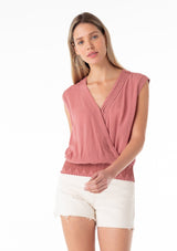 [Color: Terracotta] A half body front facing image of a blonde model wearing a bohemian resort top in terracotta pink. With short cap sleeves, a surplice v neckline, and a smocked elastic waist with embroidered stitch details. 