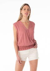 [Color: Terracotta] A front facing image of a blonde model wearing a bohemian resort top in terracotta pink. With short cap sleeves, a surplice v neckline, and a smocked elastic waist with embroidered stitch details. 