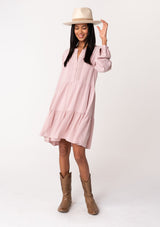 [Color: Vintage Rose] A full body front facing image of a brunette model wearing a linen blend pink baby doll mini dress. Features delicate pin tuck details, a button front, a flowy tiered skirt, and long voluminous sleeves with a button cuff closure.