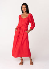 [Color: Red] A front facing image of a brunette model wearing a classic bright red bohemian maxi dress. With long sleeves, a round neckline, a button front, side pockets, and a self tie waist belt.