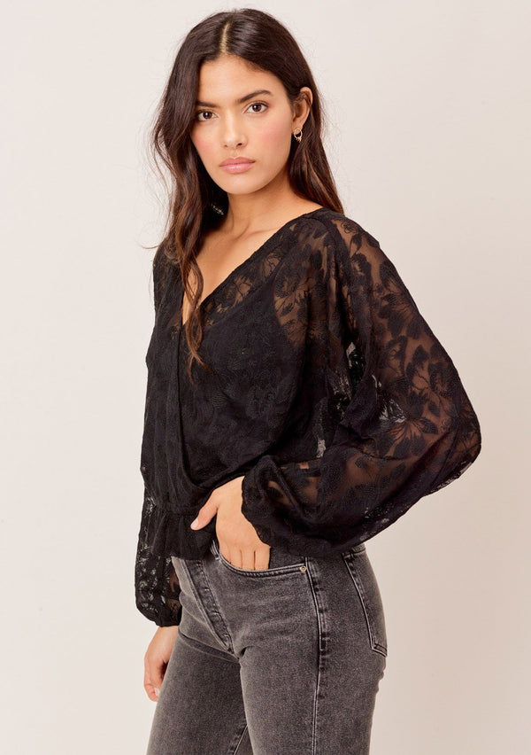 [Color: Black] A surplice front blouse in a floral embroidered lace. Featuring flattering voluminous dolman sleeves, a relaxed silhouette, and a flirty ruffled hemline. 