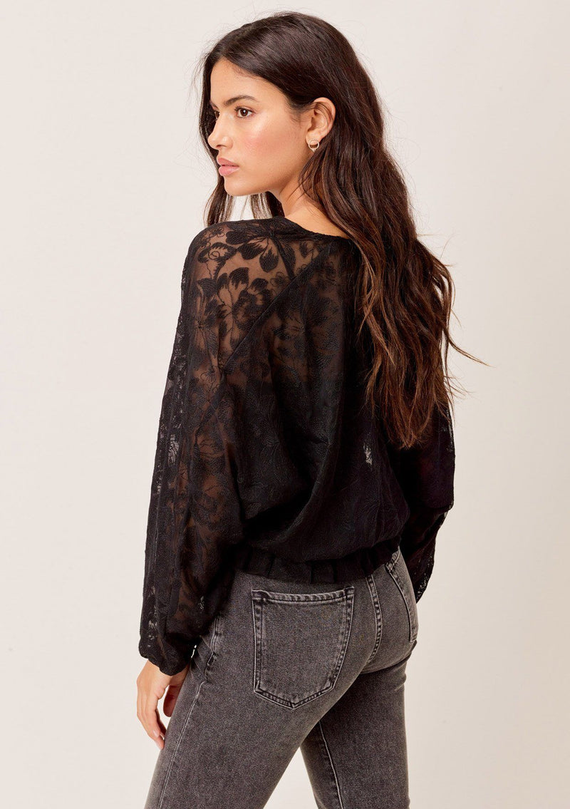[Color: Black] A surplice front blouse in a floral embroidered lace. Featuring flattering voluminous dolman sleeves, a relaxed silhouette, and a flirty ruffled hemline. 