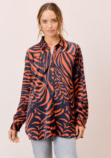[Color: Dark Teal/Toffee] A front facing image of a brunette model wearing a statement blouse with a orange and blue zebra print, button front, collared neck, and a relaxed, oversized fit.