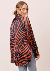 [Color: Dark Teal/Toffee] A back facing image of a brunette model wearing a statement blouse with a orange and blue zebra print, button front, collared neck, and a relaxed, oversized fit.
