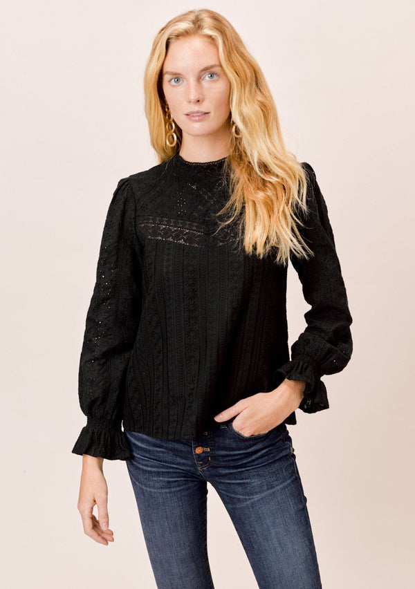 [Color: Jet Black] A blonde model wearing a black long sleeve Victorian style top with eyelet, mixed trim, mocked neckline, and smocked cuffs. 