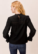 [Color: Jet Black] A blonde model wearing a black long sleeve Victorian style top with eyelet, mixed trim, mocked neckline, and smocked cuffs. 