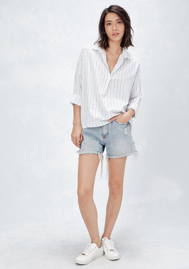 [Color: Natural/Red/Blue] A front facing image of a brunette model wearing a yarn dyed stripe shirt with subtle red stripe accents. Featuring a classic collar neckline, 3/4 length rolled sleeves, and a high low hemline. A relaxed and cool shirt for the warmer weather. 