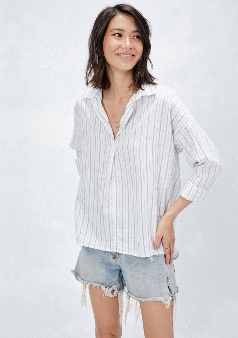 [Color: Natural/Red/Blue] A front facing image of a brunette model wearing a yarn dyed stripe shirt with subtle red stripe accents. Featuring a classic collar neckline, 3/4 length rolled sleeves, and a high low hemline. A relaxed and cool shirt for the warmer weather. 