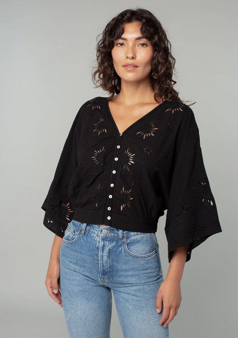 [Color: Black] A front facing image of a brunette model wearing a bohemian black embroidered eyelet top with billowy half length sleeves, a button front, and a v neckline.