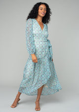 [Color: Cream/Navy] A front facing image of a brunette model wearing a flowy sheer chiffon bohemian maxi wrap dress in a navy blue and cream floral print. With long sleeves, a ruffle trimmed high low skirt, a v neckline, and a side tie waist closure. 