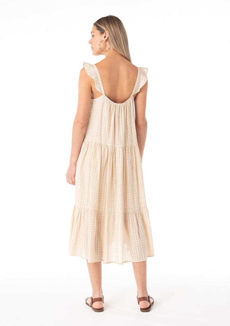 [Color: Natural] A back facing image of a blonde model wearing a casual bohemian mid length dress in a natural cotton seersucker check print. With adjustable ruffle straps, a scoop neckline in the front and back, side pockets, and a tiered flowy silhouette.