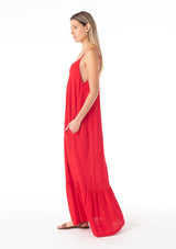 [Color: Tomato] A side facing image of a blonde model wearing a simple flowy sleeveless maxi tank dress in a bright red crinkle rayon. With a v neckline in front and back, adjustable spaghetti straps, and a tiered skirt. 