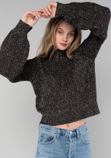 [Color: Black Multi] A front facing image of a blonde model wearing a chunky multi color knit sweater with a mock neckline and long voluminous sleeves. 