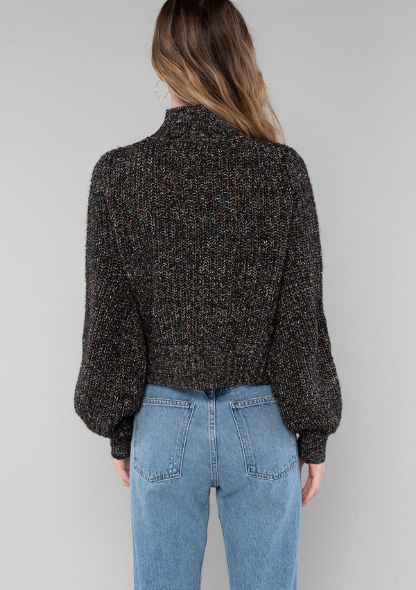 [Color: Black Multi] A back facing image of a blonde model wearing a chunky multi color knit sweater with a mock neckline and long voluminous sleeves. 