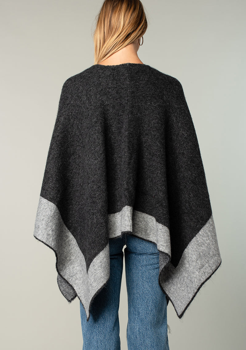 [Color: Heather Charcoal/Heather Cement] A back facing image of a blonde model wearing a soft and warm mid length sweater cape. An open front cape cardigan with a contrast border design. Perfect fall sweater, great for layering. 