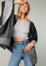 [Color: Heather Charcoal/Heather Cement] A close up front facing image of a blonde model wearing a soft and warm mid length sweater cape. An open front cape cardigan with a contrast border design. Perfect fall sweater, great for layering. 