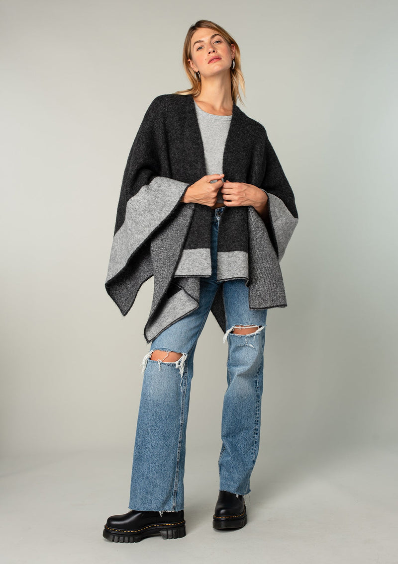 [Color: Heather Charcoal/Heather Cement] A full body front facing image of a blonde model wearing a soft and warm mid length sweater cape. An open front cape cardigan with a contrast border design. Perfect fall sweater, great for layering. 