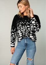 [Color: Black/Ivory] A model wearing a fuzzy black sweater in an abstract animal print. With a slightly cropped length, long sleeves, and a round neckline.