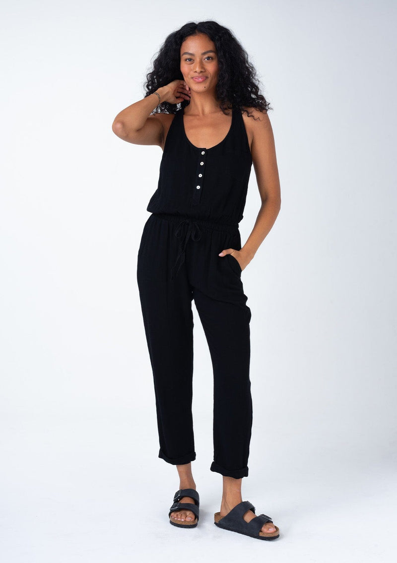 [Color: Black] A front facing image of a brunette model wearing a classic bohemian one piece black jumpsuit. With a racer back, a button front top, side pockets, a cuffed wide leg, a scoop neckline, and an elastic waist with drawstring.
