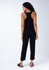 [Color: Black] A back image of a brunette model wearing a classic bohemian one piece black jumpsuit. With a racer back, a button front top, side pockets, a cuffed wide leg, a scoop neckline, and an elastic waist with drawstring.