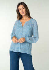 [Color: Dusty Blue/Natural] A front facing image of a brunette model wearing a sheer chiffon blouse in a blue and natural squiggle print. With long sleeves, a self covered button front, a round neckline with split v detail, and smocked elastic wrist cuffs. 