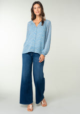 [Color: Dusty Blue/Natural] A full body front facing image of a brunette model wearing a sheer chiffon blouse in a blue and natural squiggle print. With long sleeves, a self covered button front, a round neckline with split v detail, and smocked elastic wrist cuffs. 
