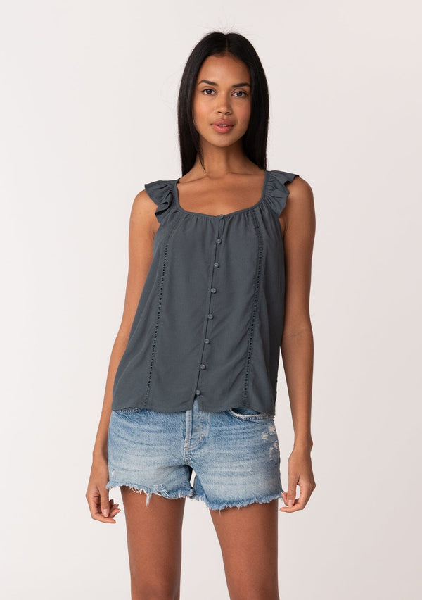 [Color: Slate] A front facing image of a brunette model wearing a slate blue summer top with short flutter straps, a scoop neckline, a button front, and lattice trim. 