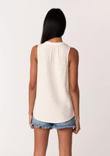 [Color: Cloud] A back facing image of a brunette model wearing a simple cotton off white tank top with a button front, a v neckline, and a relaxed fit. 
