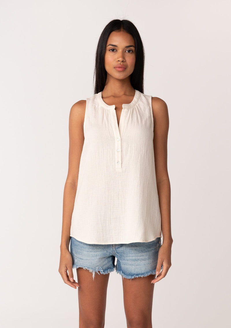 [Color: Cloud] A front facing image of a brunette model wearing a simple cotton off white tank top with a button front, a v neckline, and a relaxed fit. 