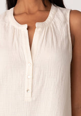 [Color: Cloud] A close up front facing image of a brunette model wearing a simple cotton off white tank top with a button front, a v neckline, and a relaxed fit. 