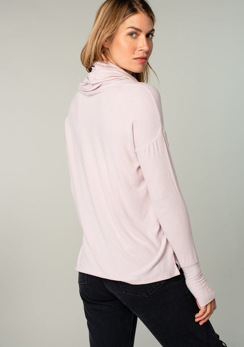 [Color: Dusty Rose] A model wearing a soft bamboo micro rib long sleeve top. Featuring an exaggerated cowl neckline that doubles as a hood, long sleeves with thumbhole accents, and breezy side vents.