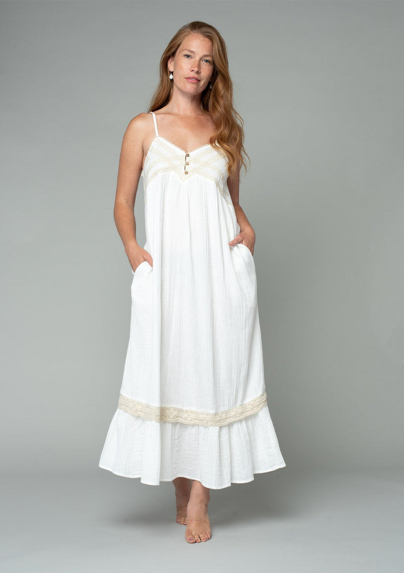 [Color: Off White/Natural] A front facing image of a red headed model wearing an off white cotton gauze sleeveless maxi dress with a natural crochet trim top and hemline. With adjustable spaghetti straps and a flowy fit.