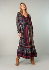 [Color: Navy/Red] A full body front facing image of a blonde model wearing a bohemian maxi dress in a navy blue and red mixed floral border print. With voluminous flared long sleeves, adjustable wrist ties, a surplice v neckline with hook and eye closure, and an elastic waist. 
