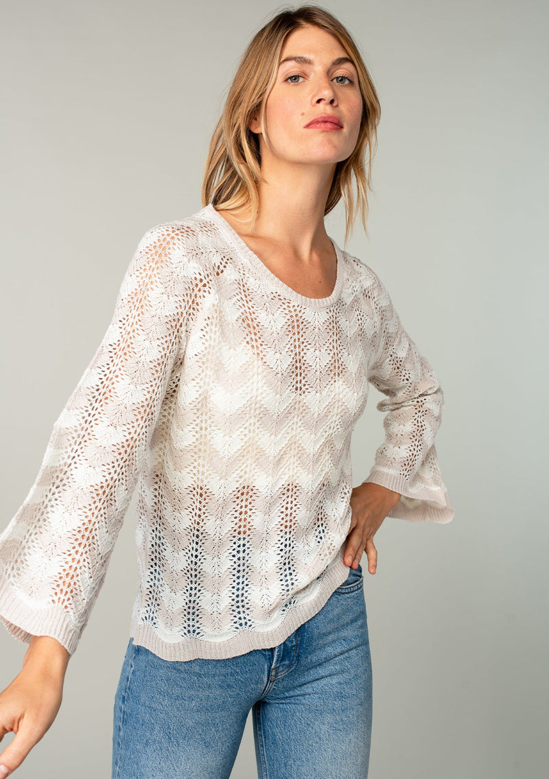 [Color: Linen/Ivory] A model wearing a beige and off white crochet knit sweater with bohemian long bell sleeves and a chevron knit pattern.